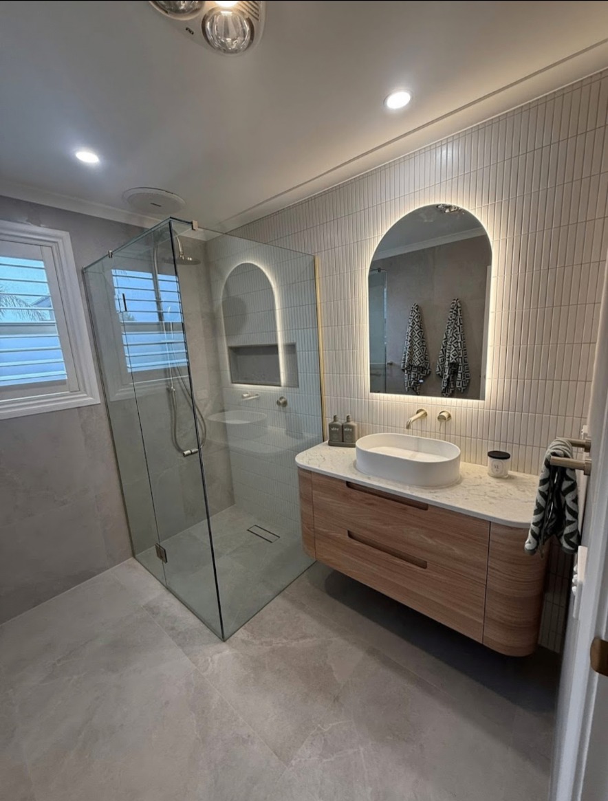 Ensuite with vertical white tiles, arched backlit mirror and stone-look floor tiles